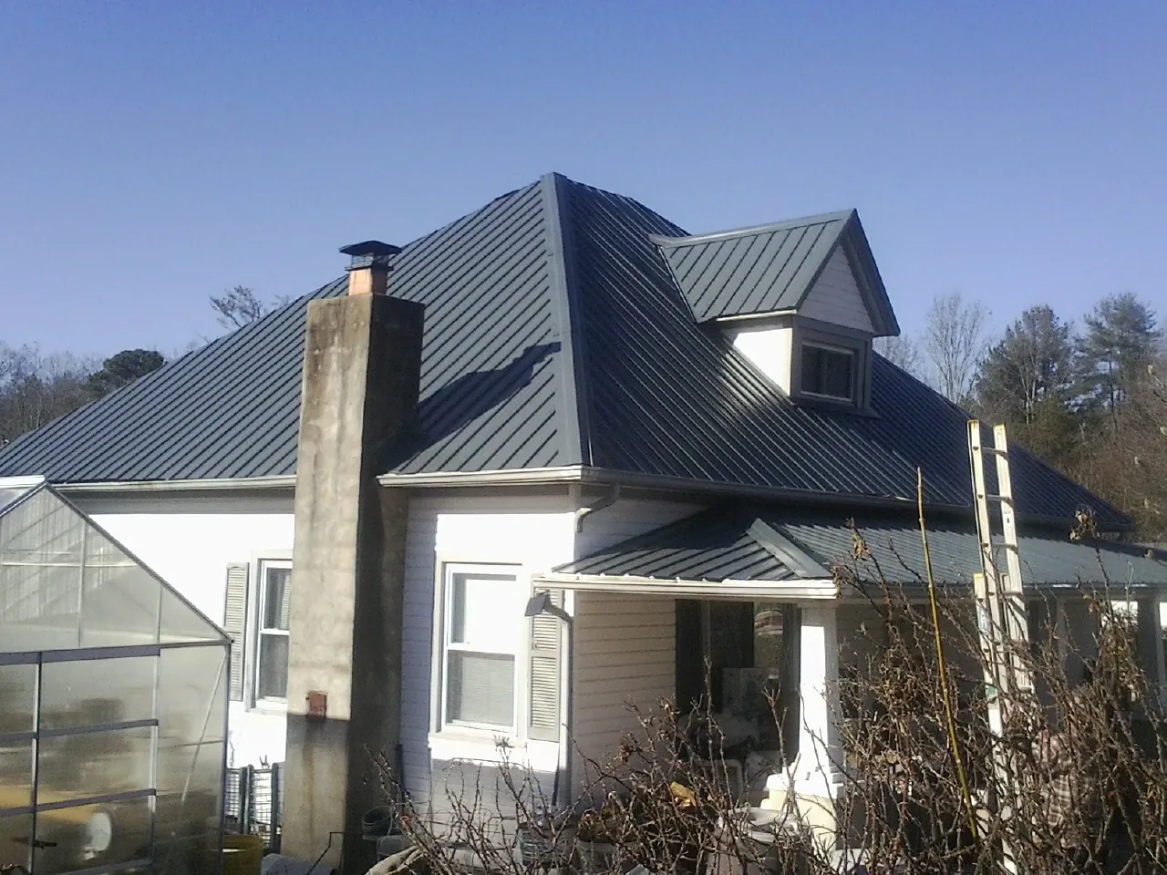 Dark blue standing seam metal roof on a white farmhouse with dormer — Slate & Tile Roof Repair by Roofing Brothers in Leakey