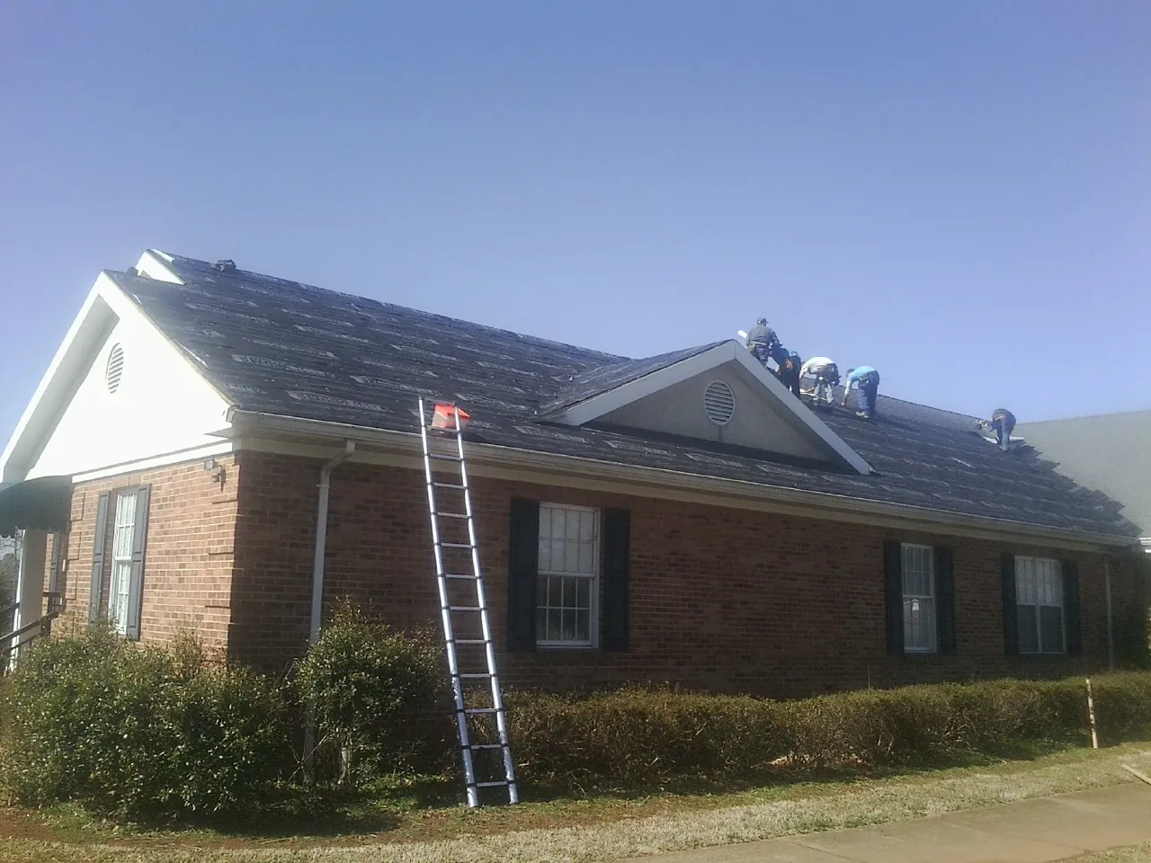 Crew tearing shingles off a brick ranch roof with a ladder set — Emergency Roof Repair work by our crew in Leakey