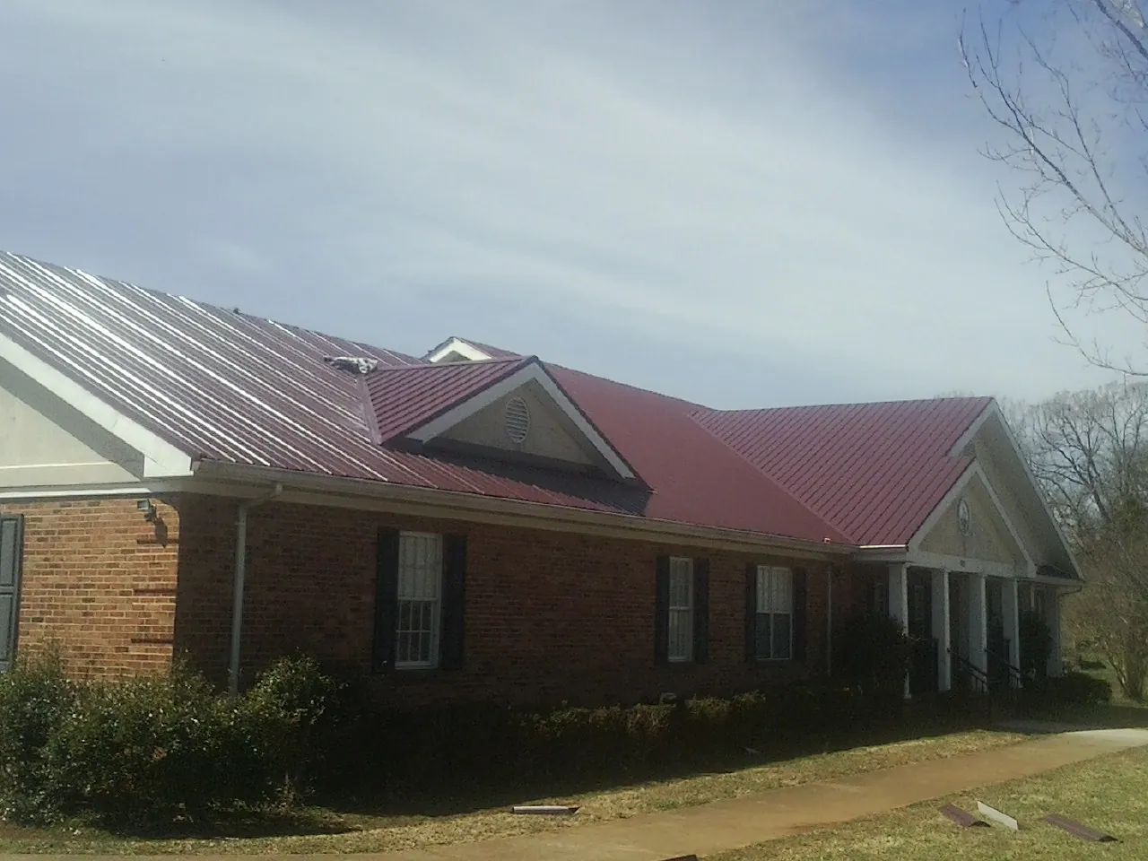 Red metal roof with gabled entries on a long brick building, from a Hail Damage Roof Repair job in Leakey