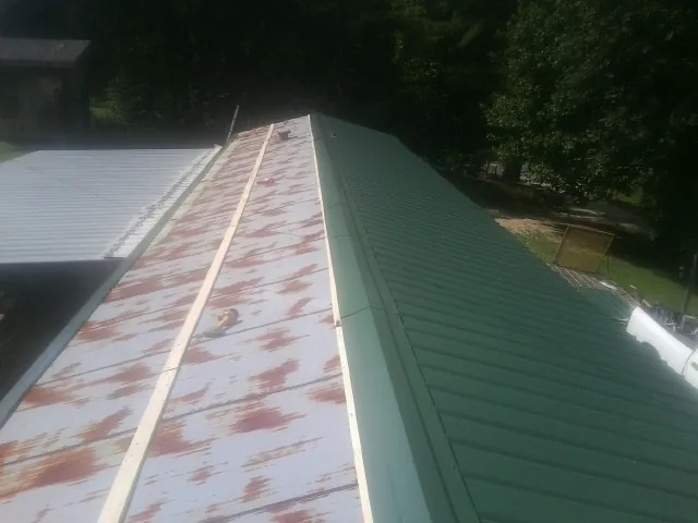 Old rusted panels beside newly installed green metal roofing — Wind Damage Roof Repair by Roofing Brothers in Leakey