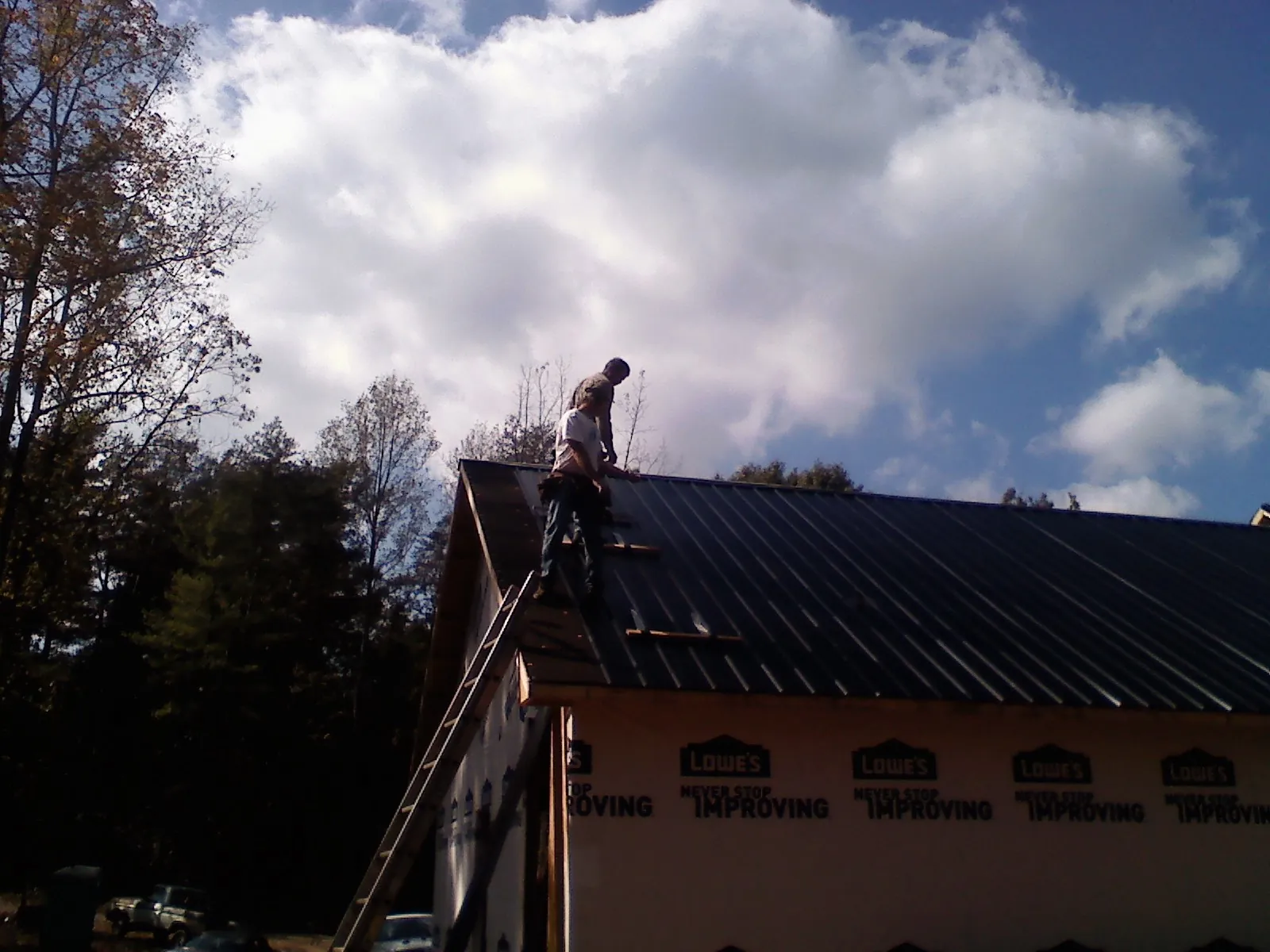 Roofer fastening dark metal panels high against a cloudy sky, from a Roof Inspection job in Leakey