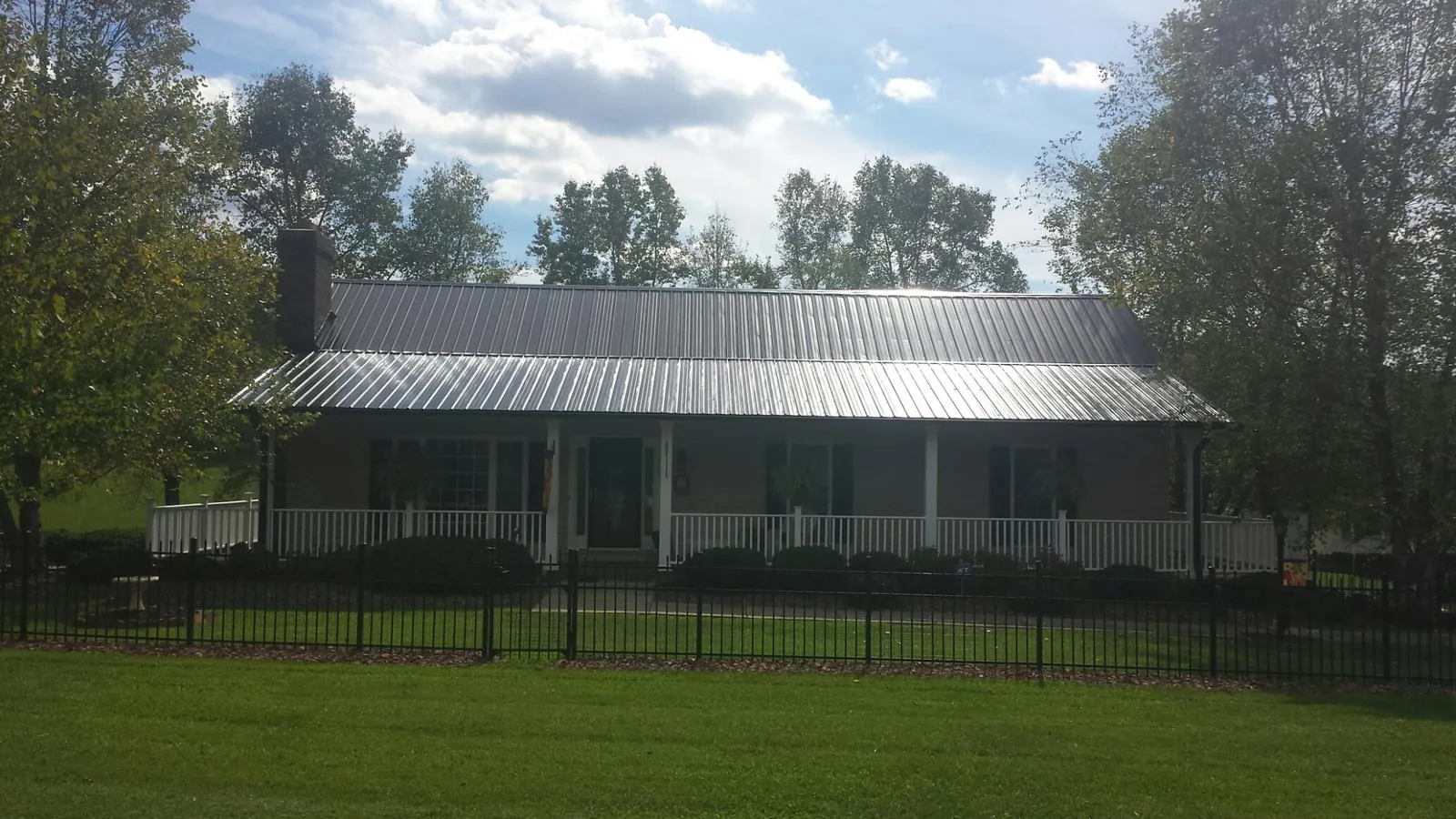 Gray metal roof on a brick ranch with a full width front porch — Gutter Guard Installation work by our crew in Leakey